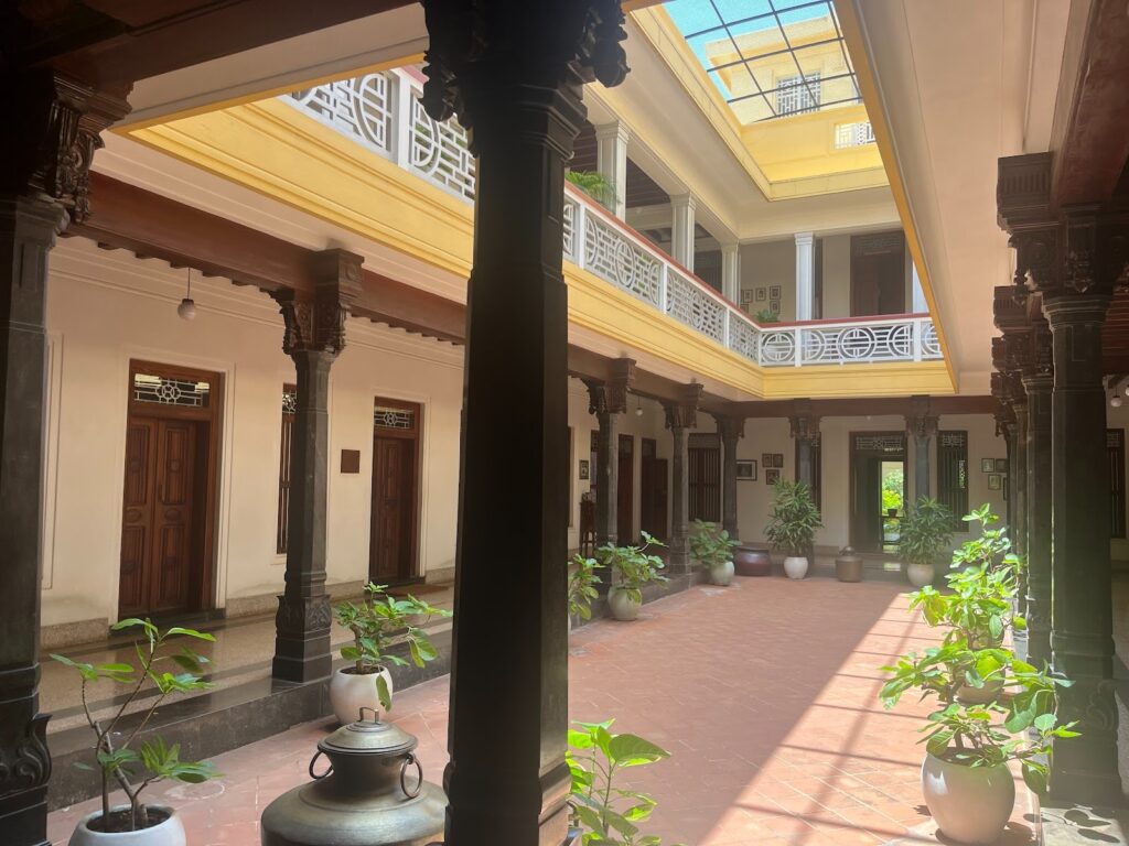 The heart of Chettinad hospitality — Visalam’s sun-drenched open courtyard, ringed by polished pillars and rooms, where gatherings, rituals, and quiet moments still unfold under
the gaze of ancestral portraits. 